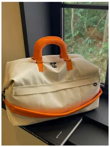 Detail shot of a stylish white travel duffel bag featuring vibrant orange handles and accents.