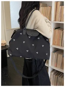 Detail view of black travel tote bag with white bow prints, top handles and strap.