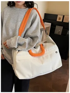 Detail view of a white travel duffel bag with orange handles, perfect for gym and short trips.