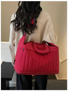 Vue arrière détaillée d'un grand sac de voyage matelassé rouge porté sur l'épaule.