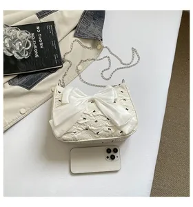 Elegant white textured underarm bag featuring a large bow and silver chain strap for women.