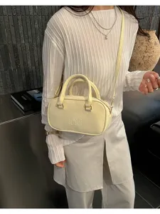 Close-up detail of a minimalist cream bowling handbag worn with a white rib-knit top
