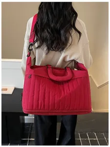 Détail de sac de voyage matelassé rouge, grand sac weekend avec bandoulière et poignée.