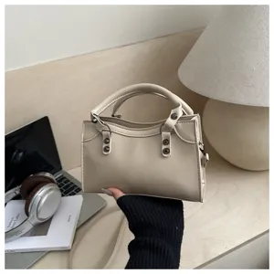Close-up of beige rivet handbag in a modern lifestyle setting with laptop and headphones