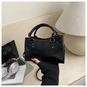 Close-up of a black glossy rivet motorcycle handbag held against a lifestyle desk background