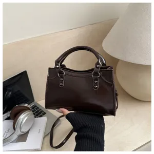 Detail of dark brown glossy rivet motorcycle bag held by hand in a lifestyle setting