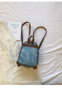 Vue arrière d'un petit sac à dos en denim rétro avec bretelles marron sur fond de tissu