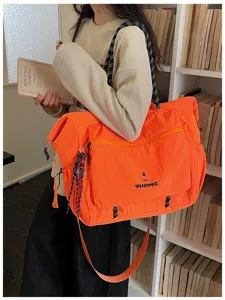 Detail shot of large capacity orange travel shoulder bag in lifestyle bookshelf setting.
