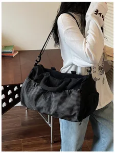 Vista detallada de la bolsa de viaje negra con bolsillo frontal a cuadros y correa.