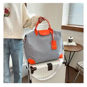 Close-up detail of the gray travel duffel bag featuring vibrant orange leather trim and handles.