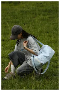 Detailed outdoor scene of a blue plaid travel bag with heart pattern worn by a model on grass.