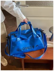 Detailed view of the vibrant blue leather gym duffel bag with handles and strap.
