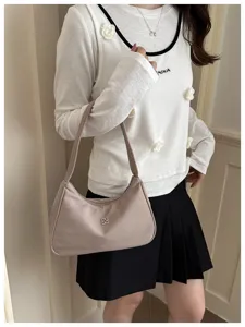 Lifestyle shot of a beige minimalist hobo shoulder bag held by a model.