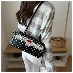 Detail view of black polka dot underarm bag with lace trim and red bow worn by model