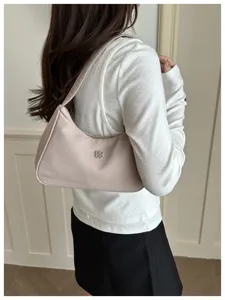 Lifestyle shot of a stylish pink underarm bag carried on the shoulder of a white sweater.