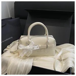 Elegante cremefarbene Bowling-Handtasche mit weißer Spitzenschleife und Perlenanhänger.