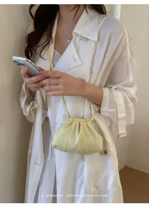 Detailed view of a yellow striped checkered cloud bag worn with a white trench coat