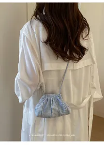 Detail of a light blue striped checked small crossbody bag worn over a white shirt.