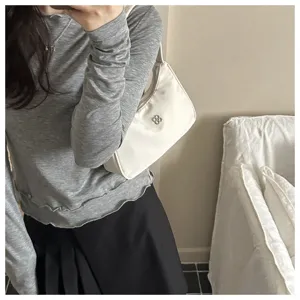 Detail view of a white minimalist shoulder underarm bag with a silver clover emblem