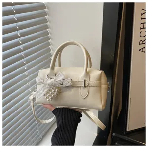 Detailansicht einer cremefarbenen Bowling-Handtasche mit weißer Spitzenschleife und Perlenherz.
