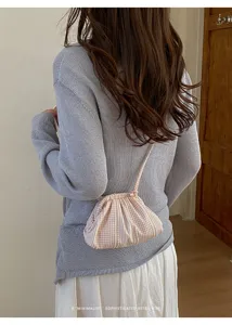 Macro detail of a small pink and white gingham drawstring crossbody bag styled on a model