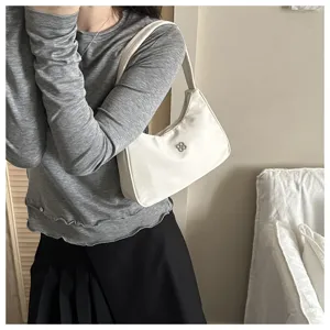 Detailed side view of a minimalist white underarm shoulder bag worn by a stylish model