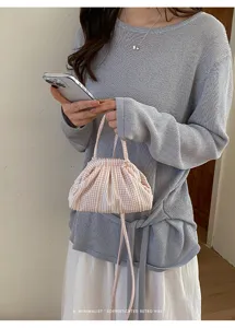 Close-up of a pink checkered mini handbag held by a model wearing a light blue knit top.