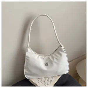 Elegant white nylon armpit shoulder bag with metallic logo detail placed on a vintage book