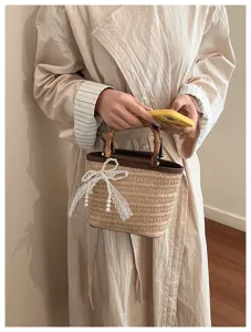 Detail einer schicken Stroh-Eimertasche mit Bambusgriff und eleganter Perlen-Schleife