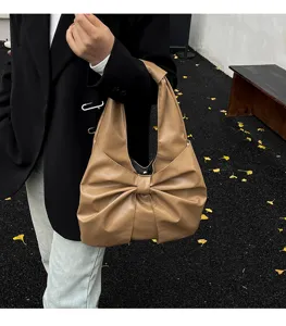 Sac cabas en similicuir marron avec grand nœud porté par un mannequin en extérieur.