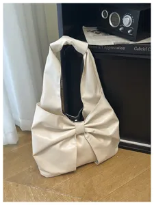 Gros plan d'un sac hobo blanc crème avec un nœud décoratif sur un fond de parquet en bois