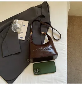 Detailed view of brown oil-wax leather hobo bag with embossed logo on a bed
