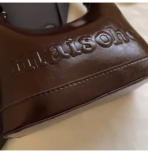 Close-up of embossed "maisohe" text on brown oil-wax leather handbag detail