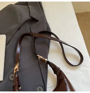 Close-up of glossy oil wax leather bag strap with elegant gold hardware detail.