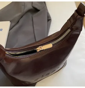 Close-up of dark brown oil-wax leather handbag featuring a smooth metal zipper detail.