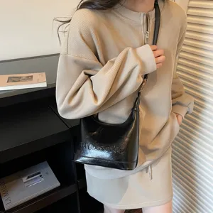 Detail of black oil-wax leather hobo crossbody bag worn with beige ribbed dress