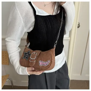 Macro view of a brown Y2K baguette underarm bag featuring star and Omg! patches