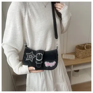 Black Y2K baguette shoulder bag with star and Omg! patches worn by a model in white dress