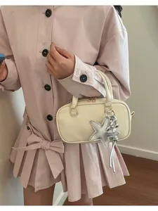 Detail view of a stylish cream Boston handbag with a silver star charm on a model