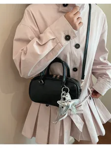 Chic black mini Boston bag with a silver star charm worn on a stylish light pink dress.