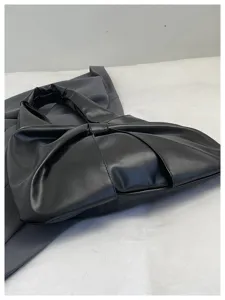 Détail d'un sac à main noir en forme de nœud montrant la texture du cuir souple