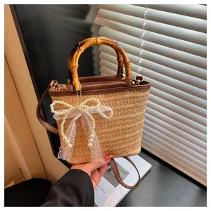 Detail einer schicken Stroh-Eimertasche mit natürlichem Bambusgriff und dekorativer Perlschleife