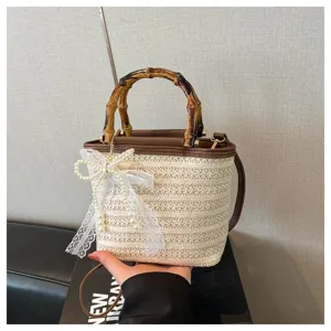 Detail einer gewebten Stroh-Eimertasche mit Bambusgriff und weißer Spitzenschleife.