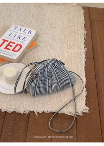 Close-up of the stylish pleated striped plaid crossbody bag on a textured cream rug