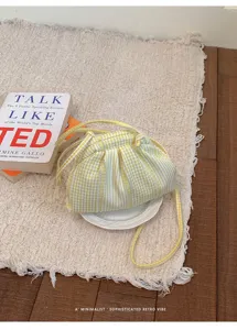 Trendy yellow and white gingham pleated small crossbody bag displayed on a cream textured rug