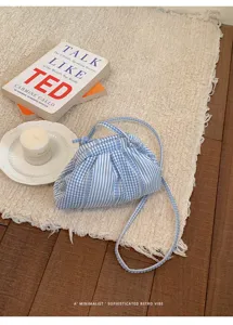 Detailed view of light blue striped and checkered crossbody bag on a textured rug