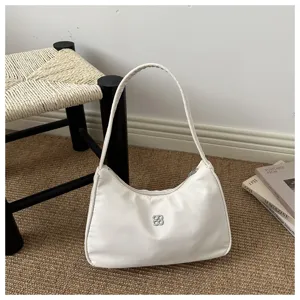 Close-up of a white minimalist underarm shoulder bag featuring a silver flower logo hardware