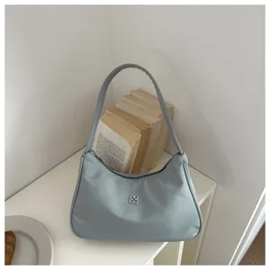 Detailed shot of a light blue minimalist underarm shoulder bag with silver metal logo