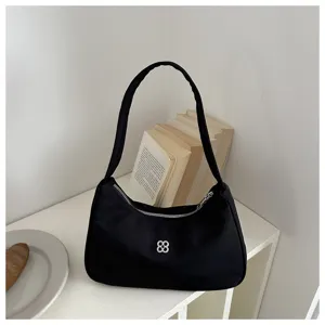 Detailed view of black minimalist underarm bag with elegant silver flower logo charm
