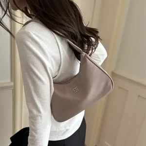 Minimalist beige underarm shoulder bag for women with decorative metal logo on front.